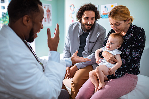 male doctor making faces with child held by parents