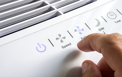 Hand about to select the fan speed on a portable air cleaner. Options for power, “auto” mode, dimming the display, and a timer are also shown.