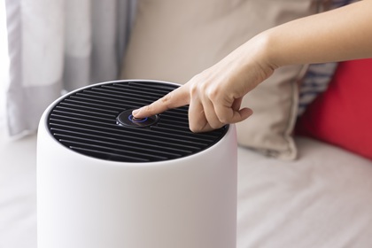 Hand pushing the top button of a portable air cleaner in someone’s home.