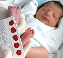 Infant with red blood spot screening card in foreground