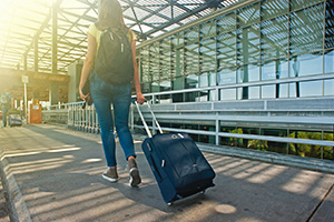 girl at airport wearing backpack pulling suitcase