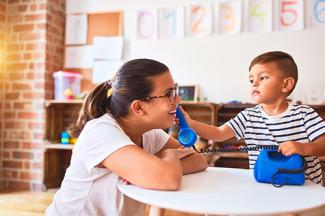 female teacher playing with toy telephone held by child