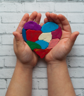A child holding a multi-color clay heart.